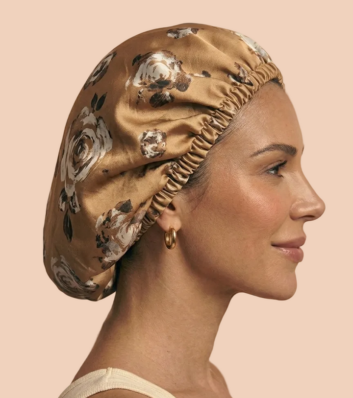 A woman in profile wearing a silk bonnet with a floral print in beige, brown, and white, set against a solid beige background.